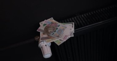 Tüm tüketiciler için ısıtma enerjisinin fiyatında keskin bir değişiklik. Bir kadın radyatöre kağıt faturalar yapıştırıyor..