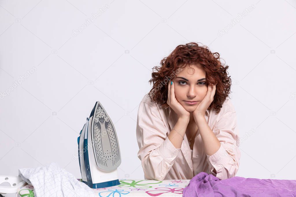 A young girl sits at the ironing board and iron. Curly short and dark