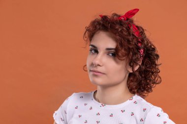 Beautiful girl stands and looks straight into the camera. Background in solid brick color. Curly hair in chestnut color.