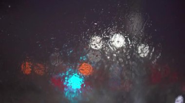 The changing light at the intersection. Rain drops float on the glass in small streaks. The foreground blurred with a photographic bokeh effect.