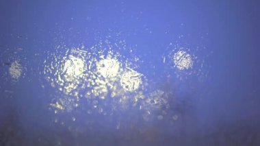 White lights seen through a wet windshield. Rainy and cloudy weather. Unstable focus. The foreground blurred. Photographic effect of bokeh.