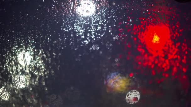曇りの日に雨が窓ガラスの下に落ちる 2番目の前景ボケ効果でぼやけている 濡れたフロントガラスと輝くライト 赤信号 — ストック動画