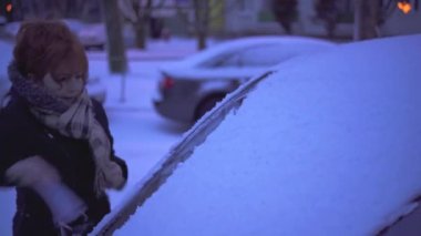 Winter season in the eastern part of Europe. Heavy snowfall forces drivers to shovel snow from their cars. A woman wearing a winter jacket and scarf.