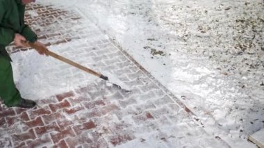 A worker quickly clears snow from a wide section of sidewalk laid with paving stones. The winter season brings snow and frost. A manual worker at work.
