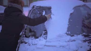 Winter season in the eastern part of Europe. Heavy snowfall forces drivers to shovel snow from their cars. A woman wearing a winter jacket and scarf.