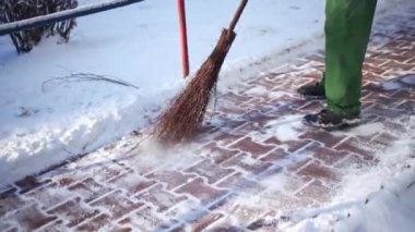 Sweeping movements with a wooden broom. The host of the property cleans the snow from the paving stones. A manual worker while performing cleaning work.