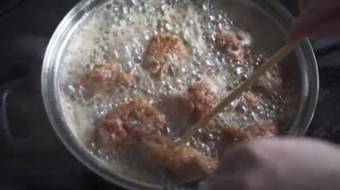 Breaded pieces of chicken are fried in hot oil. A stainless steel skillet stands on a hot stove top. Deep frying.
