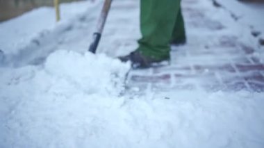 An area host removes piled snow from paving stones. A worker in work clothes clears the area on the citys estate of frozen snow.