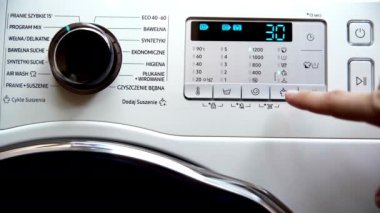 The man changes the degree of drying of the clothes after completing the laundry with the program set - mix. He presses with his finger on the button with the pictogram drying.