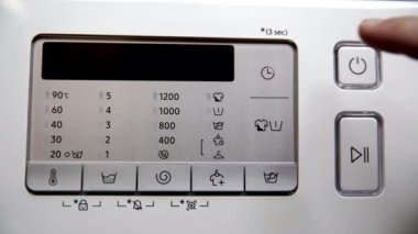 A man uses the power key to turn on a home automatic washing machine. A close-up view of the washing machines control panel.