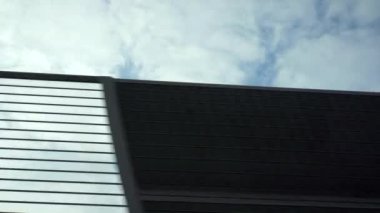 White clouds in the blue sky are slowly moving. The view from a speeding car just outside the sound fence.