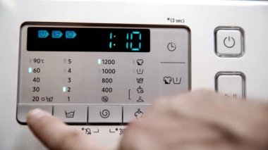 Close-up view of the control panel of a home automatic washer-dryer. A man uses a button to set the desired temperature for washing clothes.