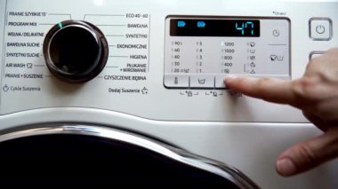 The man changes the spin speed of the laundry on the set program - mix. He presses with his finger on the button with the pictogram spinning.