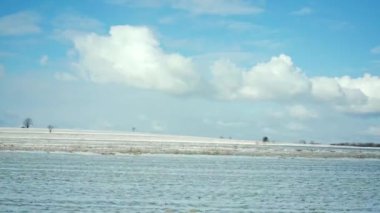 A plowed agricultural field covered with a layer of white snow seen while traveling through the side window of a car. The winter season in the countryside.