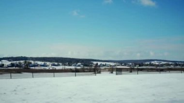 A view of a rural settlement during the winter season. Agricultural fields and village buildings covered with white snow up to the horizon. A sunny day in winter.