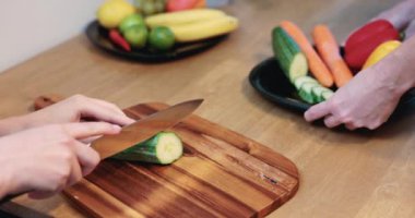 Autumn colored vegetables cut on a brown board. Person slices peppers and carrots with a sharp knife. Preparing healthy meal at home. Meal at home with friend. Colorful vegetables and fruits.