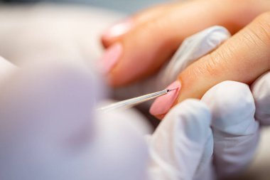 Ön planda bulanıklık. İki kadının elinde büyük bir yakın çekim. Güzellik salonunda güzellik uzmanının hizmetinden zevk alan bir kadın. Profesyonel melez manikürü müşterilerin ellerinde yapılıyor..