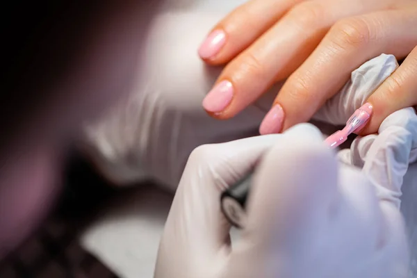 stock image A beautician paints the nail of the index finger. A woman using the services of a manicurist. The beautician paints the clients nails pink. Applying a layer of hybrid varnish.