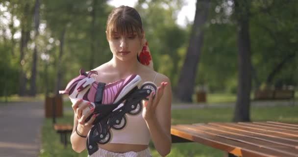 一个年轻人坐在公园的长椅上 穿着一件紧身衣 这个女孩笑着提起一把轮轴 转动着一个橡胶轮 — 图库视频影像