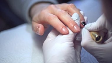 Bir manikürcü tek kullanımlık lateks eldiven giyer. Bir kadın müşterisinin tırnaklarını boyuyor. Güzellik salonundaki bir müşteriyle ilgilenmek. Bir güzellik uzmanı elle tırnak boyama yapar. Doğal bir tırnak tabağı boyuyorum..