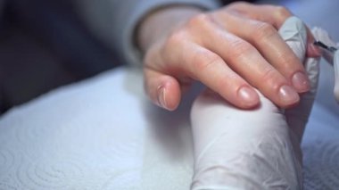 Güzellik uzmanı müşteri kabul eder. Bir manikürcü bir kadının tırnaklarını boyuyor. Güzellik salonunun hizmetlerinden yararlanarak. Temiz ojeyle oje sürüyorum. Kuaföre çivi tabanlı manto sürüyorum..