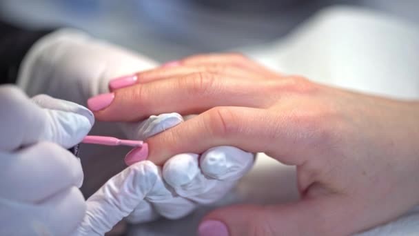 一个女人去美容院 用粉红的指甲油修指甲 美容师和病人的手部特写 用一次性乳胶手套工作 — 图库视频影像