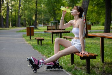 Yeşil bir şehir parkında vakit geçirmek. Genç bir kadın bankta oturur ve şişeden içer. Doğada sıcak bir gün. Sporcu antrenman sırasında bir bankta otururken dinleniyor