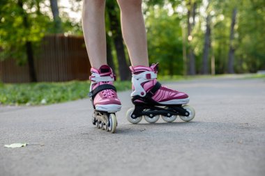 Patenci kız parkta paten kayıyor. Modaya uygun mor ve gri renkte patenler. Spor aletleri çok uygun. Açık havada spor yapmak..