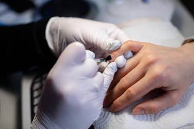 Güzellik salonunun müşterisi hibrit manikür hizmeti sunar. Doğal tırnak cilası için melez cilası uygulaması. Daha fazla kozmetik işlem için tırnak plakasını hazırlıyorum..