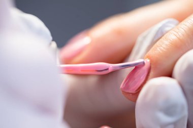 Güzellik salonunda hijyen prensiplerini korumak. Güzellik uzmanı müşterinin işaret parmağını elinde tutuyor. Tırnakların boyandığı yakın plan bir fotoğraf. Melez manikür hizmeti veriliyor..