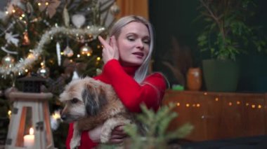 The girl is stroking the dog she is holding in her arms while talking. Christmas decoration of the apartment.