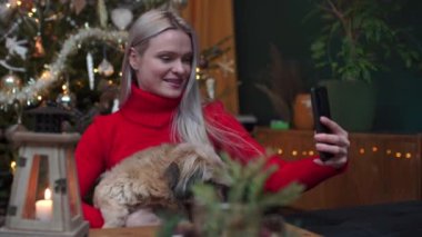 Çekici bir kadın köpeğiyle birlikte bir video bloğu kaydediyor. Noel evi dekorasyonu.
