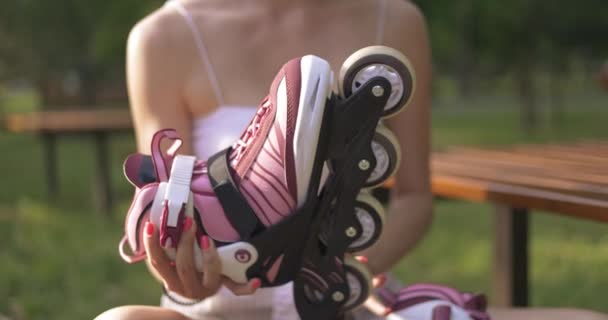 一个穿着无袖衬衫的女孩坐在公园的长椅上 面前拿着一把轮滑刀片 她在纺橡胶轮 粉红色和紫色阴影的轮轴 上有旋转的橡胶轮 — 图库视频影像