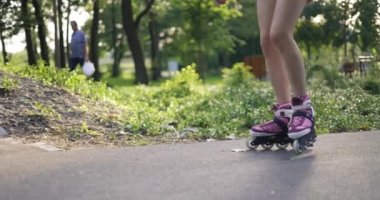 Genç bir kız güneşli, yeşil bir parkta paten kayıyor. Asfalt bir sokakta kayıyor, bir rampanın yanından geçiyor ve numaralar yapıyor. Arka planda, çantalı bir adam arka planda yürüyor..