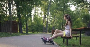 Genç yorgun bir kız parkta bir bankta oturuyor. Kız paten kaydıktan sonra dinleniyor. Sarı izotonik içeceği olan bir şişe tezgahın üzerinde duruyor. Arka planda bulanık ağaçlar ve bir sürü...