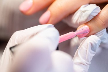 Ön planda bulanıklık. Çalışan bir manikürcünün eline yakın çekim. Güzellik uzmanı melez manikürü yapıyor. Profesyonel kadın tırnaklarını pembeye boyar..