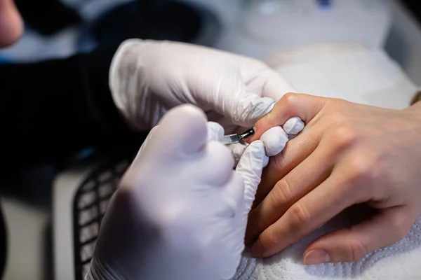 Preparation of the nail plate for further cosmetic procedures. The beautician wears disposable nitrile gloves. Maintaining the rules of hygiene in the beauty salon.