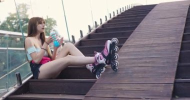 Genç bir kadın tahta merdivenlerde bacakları düz oturuyor. Kız bir şişeden izotonik mavi bir içecek içiyor. Egzersiz sonrası yorgun bir kadını dinlendirmek.