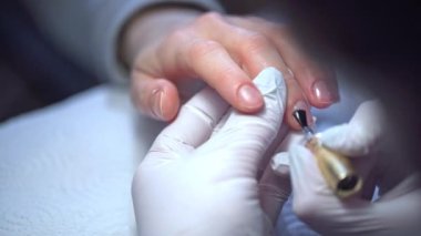Güzellik uzmanının müşterisi güzellik salonundadır. Kadın melez manikürü yaptırıyor. Manikürcü doğal tırnak plakasına bir taban manto uygular. Güzellik salonu ekipmanları.