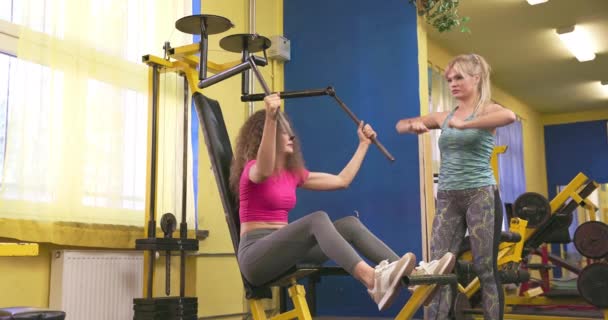 運動トレーナーの助けを借りて 機器の演習の女性 ジムでのスポーツウェアの写真の2人の女性 — ストック動画
