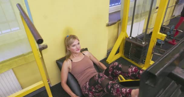 一个快乐的女人在健身房的设备上做腿操 一个穿运动服的女孩 — 图库视频影像
