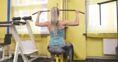 Uzun sarı saçlı kız spor salonunda egzersiz yapıyor. Klasik spor aletleri..