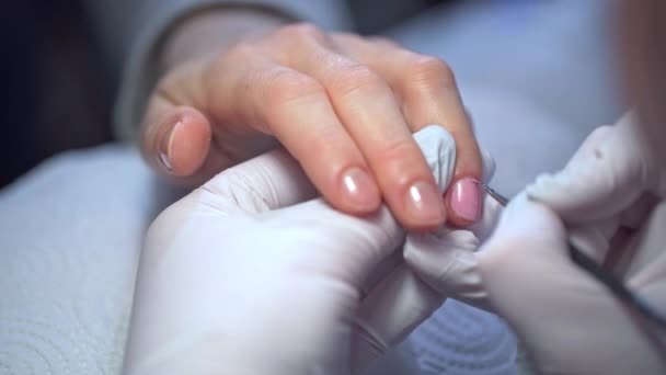 美容师用粉红的抛光剂涂女人的指甲 一个女人的特写手伸进了美容院在天然的指甲板上修指甲 涂第一层油漆 — 图库视频影像