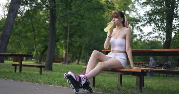 Lavičce Parku Sedí Bruslařka Kolečkovými Bruslemi Nohou Pije Láhve Dívka — Stock video