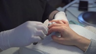 Tırnak kesen bir manikürcünün ellerine yakın çekim. Güzellik salonunun müşterisi manikür yaptırıyor. Güzellik uzmanı çalışırken lateks eldiven giyer..
