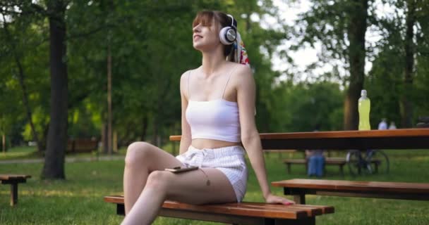 Parktaki Bankta Oturan Bir Kız Bir Kız Büyük Kablosuz Kulaklıklardan — Stok video