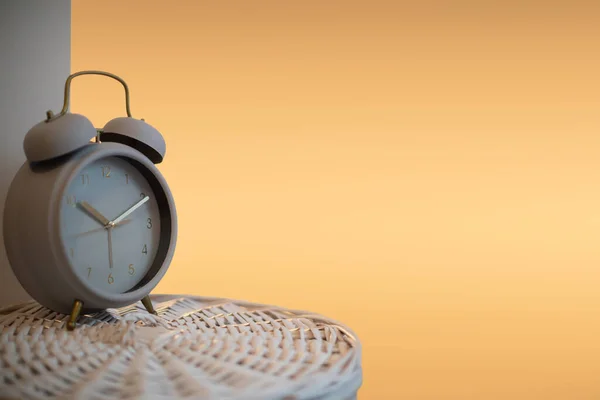 古いアナログ目覚まし時計は 織りのウィッカーバスケットに立っており 時間を示しています ぼんやりとしたオレンジ色の光は 夜に照らされたベッドサイドランプを模倣します — ストック写真