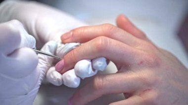 Güzellik salonunda kadınlar için profesyonel hizmet. Doğal ojeyi pembe ojeyle boyuyorum. Melez verniğin ilk katmanının uygulanması. Bir kadının ellerinin yakın plan görüntüsü.
