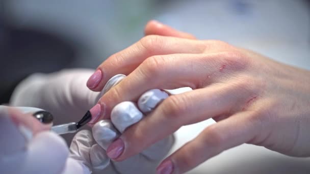美人鱼对指甲的影响由专业人士进行 把光泽涂在涂有粉红抛光的钉子上 美容师在美容院给顾客画指甲 — 图库视频影像