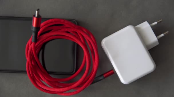 一只人类的手伸向一个白色充电器 它连接着一根红色盘绕的电缆 充电器和电缆放在手机的顶部 右手拿起充电器和电缆 左撇子 — 图库视频影像